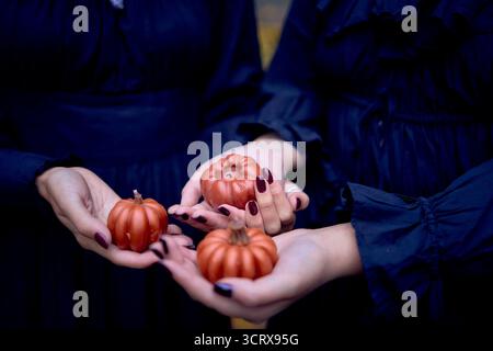Deux femmes en robes longues noires près des rochers noirs sur Halloween avec des bougies en forme de citrouilles, effectuant un rituel de sorcière, sorcière moderne Banque D'Images