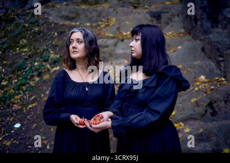 Deux femmes en robes longues noires près des rochers noirs sur Halloween avec des bougies en forme de citrouilles, effectuant un rituel de sorcière, sorcière moderne Banque D'Images