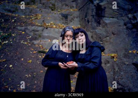 Deux femmes en robes longues noires près des rochers noirs sur Halloween avec des bougies en forme de citrouilles, effectuant un rituel de sorcière, sorcière moderne Banque D'Images