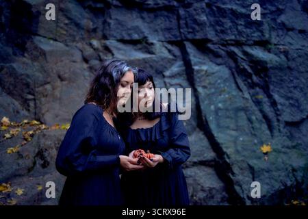 Deux femmes en robes longues noires près des rochers noirs sur Halloween avec des bougies en forme de citrouilles, effectuant un rituel de sorcière, sorcière moderne Banque D'Images