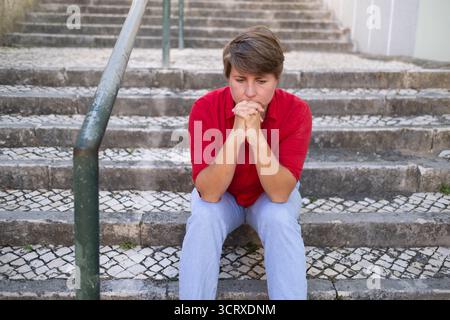 Femme européenne d'âge moyen assise sur des escaliers extérieurs se sentant triste et déprimée Banque D'Images