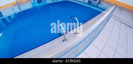 Piscine intérieure avec échelle métallique détaillée. Une piscine intérieure lumineuse et bien entretenue avec une échelle d'entrée en acier inoxydable. Banque D'Images