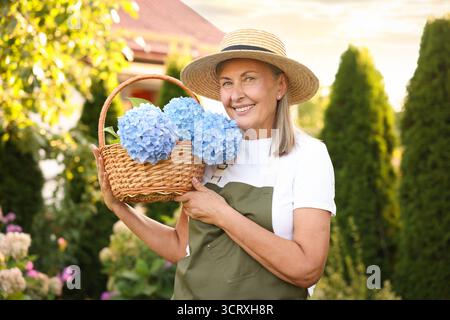 Femme senior avec panier en osier de fleurs dans le jardin Banque D'Images