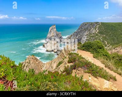 Ursa Beach près de Cabo da Roca vue de dessus présente des falaises accidentées, des vagues turquoise de l'océan, et un éperon rocheux. Une végétation luxuriante et succulente borde le sentier sablonneux Banque D'Images