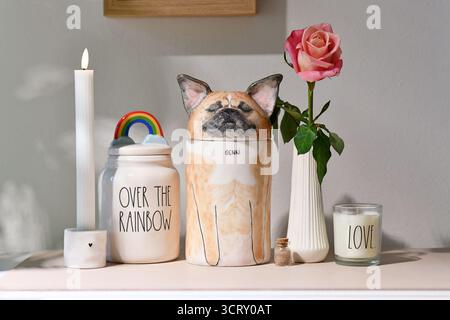 Allemagne - 30 août 2025 : urne pour chien de compagnie personnalisée en forme de bouledogue français entourée d'une bougie et d'une fleur de rose. Mémorial décoratif pour chiens Banque D'Images