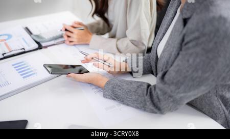 Les femmes asiatiques professionnelles collaborent en examinant les statistiques du marché et les rapports d'entreprise sur un tableau blanc. Ils élaborent des stratégies en utilisant des appareils. Banque D'Images