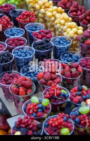 Une exposition invitante de diverses baies fraîches, y compris des bleuets, des framboises, des fraises et des mûres, portionné dans des gobelets en plastique sur un marché. Banque D'Images