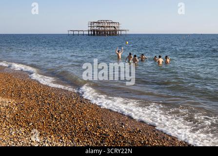 Groupe de jeunes hommes jouant dans la mer avec Brighton West Pier Behind, Brighton, East Sussex, Angleterre, Royaume-Uni, Europe Banque D'Images