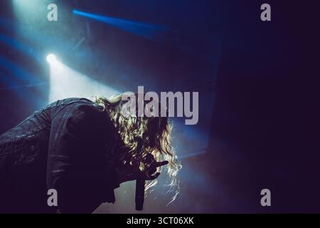 Chanteur métal se produisant passionnément sur scène lors d'un spectacle de club, avec un éclairage dramatique coloré Banque D'Images