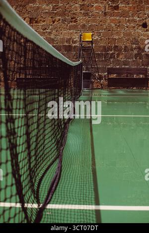 Court de tennis à Héraklion, en Grèce, avec un filet centré, un fauteuil arbitre jaune et un mur de pierre en toile de fond, capturant un mélange tranquille de sport et d'archite âgé Banque D'Images