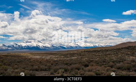 Paysage désertique d'avril dans le Nevada avec broussailles au premier plan, montagnes enneigées et ciel nuageux avec une lumière douce et des taches bleues. Banque D'Images