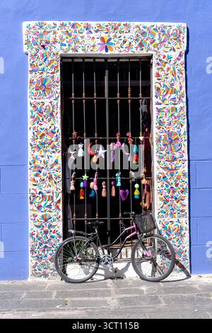 Un vélo coloré est garé devant une porte colorée. Le vélo est noir et a un panier rose. La porte est décorée avec des motifs colorés. La scène Banque D'Images
