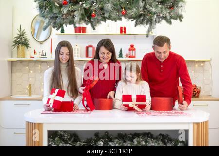 Famille ouvrant des cadeaux de Noël dans la cuisine festive. Une famille joyeuse de quatre ouvre des cadeaux de Noël dans une cuisine décorée, mettant en vedette des vacances Banque D'Images