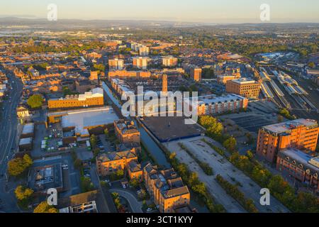 Vue aérienne matinale de Chester, Royaume-Uni, mettant en évidence le canal traversant la ville, une grande cheminée historique, des entrepôts et des logements en briques rouges. Banque D'Images