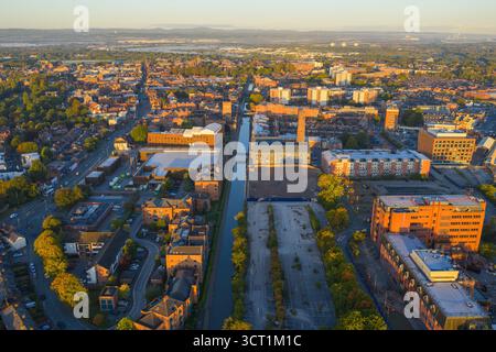 Vue aérienne matinale de Chester, Royaume-Uni, mettant en évidence le canal traversant la ville, une grande cheminée historique, des entrepôts et des logements en briques rouges. Banque D'Images