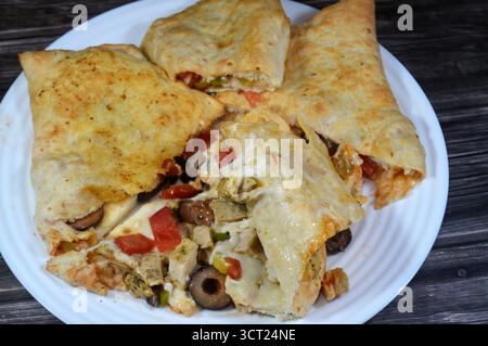 Une assiette de sandwich Pizza rempli de poulet avec des morceaux de tomate, poivre, olive, fromage mozzarella, sauce tomate dans un sandwich Banque D'Images