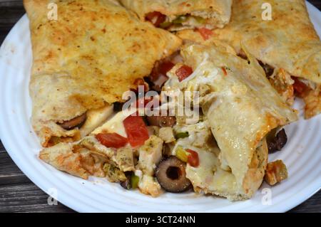 Une assiette de sandwich Pizza rempli de poulet avec des morceaux de tomate, poivre, olive, fromage mozzarella, sauce tomate dans un sandwich Banque D'Images