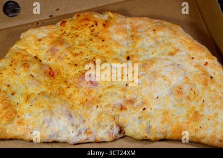 Un sandwich en forme de demi-lune, sandwich Pizza rempli de poulet avec morceaux de tomate, poivre, olive, fromage mozzarella, sauce tomate dans un demi-cercle sa Banque D'Images