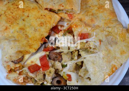 Une assiette de sandwich Pizza rempli de poulet avec des morceaux de tomate, poivre, olive, fromage mozzarella, sauce tomate dans un sandwich Banque D'Images