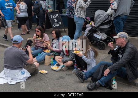 Repas de restauration rapide Fish and Chip à emporter. Des gens, un groupe familial assis sur le trottoir mangeant un repas en papier. Fish N Chips devant la boutique de plats à emporter. Corby. Northamptonshire, Angleterre 3 juin 2022 2020s UK HOMER SYKES Banque D'Images