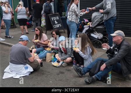 Repas de restauration rapide Fish and Chip. Des gens, un groupe familial assis sur le trottoir mangeant des Fish N Chips. Corby. Northamptonshire, Angleterre 3 juin 2022 2020s UK HOMER SYKES Banque D'Images
