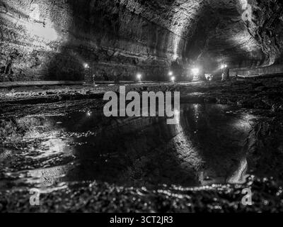 Dans la grotte de Mangjanggul, Jeju, une figure solitaire dans un se dresse devant le tunnel sur le sol rocheux à côté d'une flaque reflétant la grotte de lave toute litée Banque D'Images