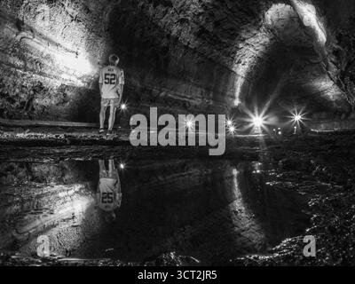 Dans la grotte de Mangjanggul, Jeju, une figure solitaire dans un se dresse devant le tunnel sur le sol rocheux à côté d'une flaque reflétant la grotte de lave toute litée Banque D'Images