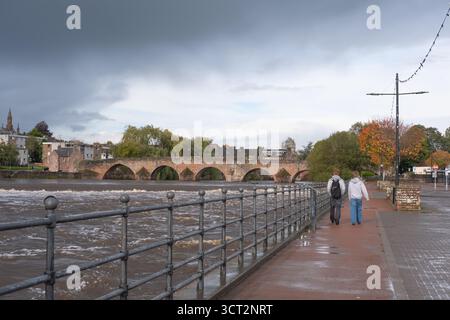 4 octobre 2025, Dumfries, Écosse, deux personnes marchent le long de la rivière Nith dans les Whitesands après la tempête Amy. Ciel orageux visible. Banque D'Images