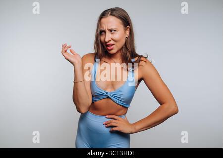 Une jeune femme montre une tenue bleue tendance, posant de manière ludique avec ses mains. Elle a une expression confiante, debout dans un studio bien éclairé. Le dos Banque D'Images
