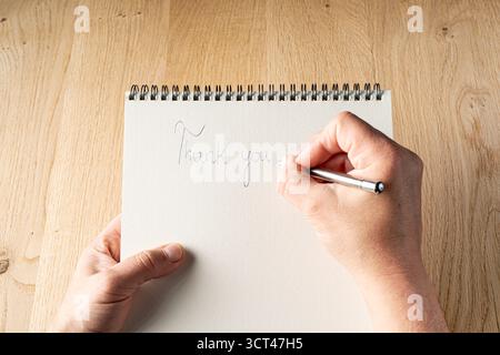 Une personne écrit une note de remerciement sur un cahier à reliure spirale. La personne utilise un stylo pour écrire la note Banque D'Images