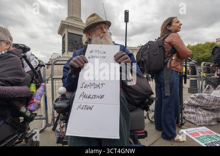 Londres, Royaume-Uni. 4 octobre 2025. Un homme âgé avec une longue barbe blanche et des lunettes est assis dans un fauteuil roulant avec une pancarte manuscrite indiquant « PLUS DE GÉNOCIDE – je SOUTIENS À NOUVEAU LA PALESTINE » lors d’une manifestation publique. Vêtu d'un chapeau et de gants, il est entouré d'autres manifestants, dont certains sont également en fauteuil roulant. Défendre nos jurys organisent une manifestation non violente à Trafalgar Square. La manifestation vise à lever l'interdiction de Palestine action, qui a été interdite en tant que groupe terroriste en juillet 2025 en vertu de la loi britannique de 2000 sur le terrorisme. Penelope Barritt/Alamy Live News Banque D'Images