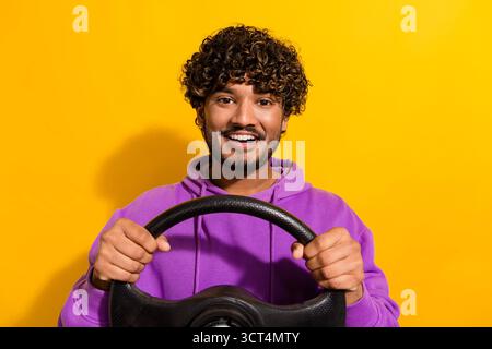 Jeune homme souriant dans un sweat à capuche violet tenant un volant sur un fond jaune vif Banque D'Images