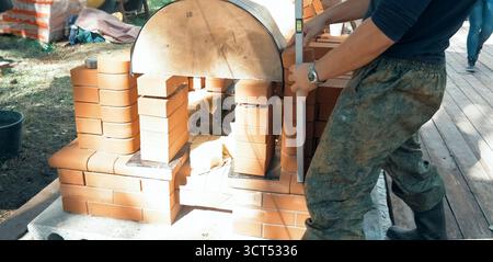 Un homme construit un mur de briques. Brique mise sur la solution. Construction d'une maison en brique. Banque D'Images