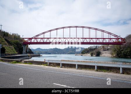 Pont Red Arch au-dessus de la voie navigable au Japon. Pont en arc d'acier rouge vif enjambant une rivière bleu calme contre des paysages de montagne au Japon. Banque D'Images