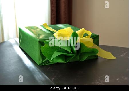 Cadeau enveloppé dans du papier vert avec ruban jaune sur la table Banque D'Images
