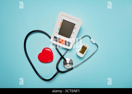 Stéthoscope, modèle cardiaque, pilules et appareils numériques sur fond bleu pâle symbolisant l'amour et les soins dans le domaine médical. Banque D'Images