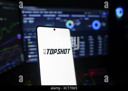 Smartphone affichant le logo NBA Top Shot contre les graphiques financiers sur les moniteurs Banque D'Images