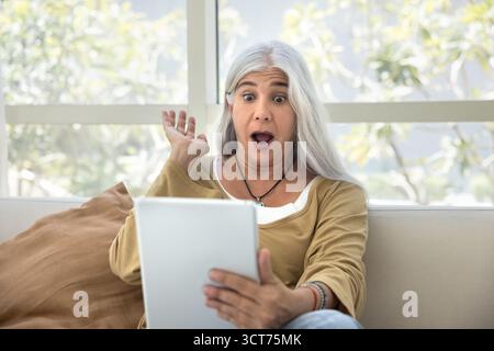 Femme âgée choquée regardant du contenu en ligne sur tablette Banque D'Images