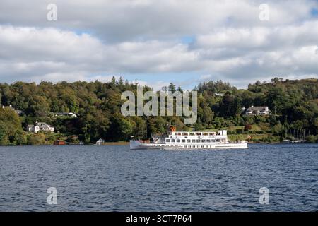 Traversier blanc de passagers naviguant à travers le lac Windermere avec des collines boisées et des maisons au bord du lac en arrière-plan, Lake District, Cumbria, Angleterre Banque D'Images