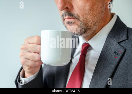 Gros plan de l'homme d'affaires tenant la tasse de café blanc près de la fenêtre du bureau, la routine du matin et le style de vie du lieu de travail. Mise au point sélective. Banque D'Images