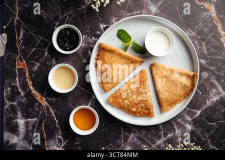 Crêpes minces bliny avec sauces assorties sur table en marbre Banque D'Images