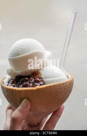 Crème glacée à la main sundae dans une coquille de noix de coco avec des cuillères à noix de coco et une garniture de haricots rouges Banque D'Images