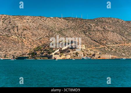 Vue panoramique sur la forteresse de l'île de Spinalonga en Crète, Grèce, entourée par la mer turquoise avec des bateaux touristiques et des collines rocheuses en arrière-plan, populaire Banque D'Images
