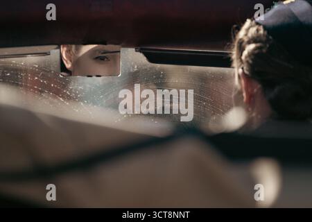 Oeil de femme réfléchi dans le rétroviseur de la voiture avec des gouttes de pluie sur le pare-brise Banque D'Images