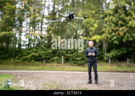 Drone blanc en vol avec opérateur tenant la télécommande dans une zone boisée Banque D'Images