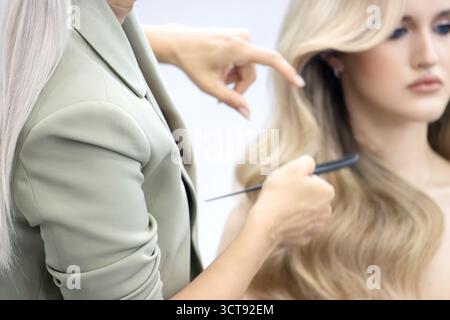 Coiffeur styliste coupant ou ajustant les cheveux blonds longs du client. Service de beauté professionnel Banque D'Images