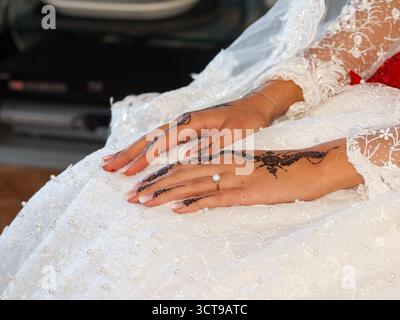 Mains de mariée décorées de henné reposant sur une robe de mariée brodée de perles blanches. Banque D'Images