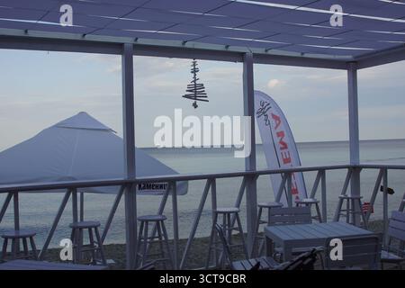 Vue sur la côte depuis un café en bord de mer avec parasols blancs et tabourets de bar au premier plan pendant une journée calme Banque D'Images