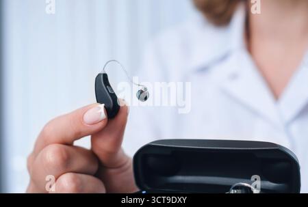 Aide auditive de charge de patient dans un chargeur intelligent portable spécial avec banque d'alimentation intégrée. Étui dans les mains de l'homme garde les aides auditives au sec et en toute sécurité Banque D'Images