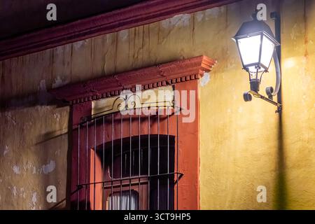 Une fenêtre avec une barre métallique est éclairée par un lampadaire. La lumière projette une lueur chaude sur le bâtiment. Centre historique de Queretaro, architecte colonial Banque D'Images
